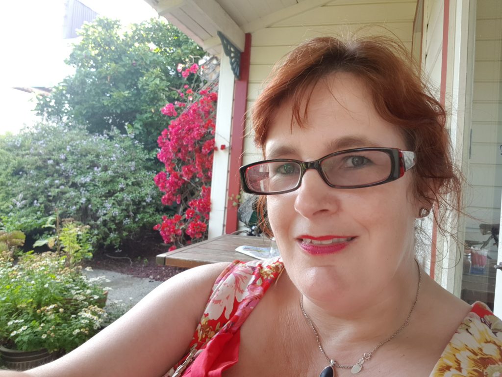 image of kitty smiling into the camera with red flowers in the background.