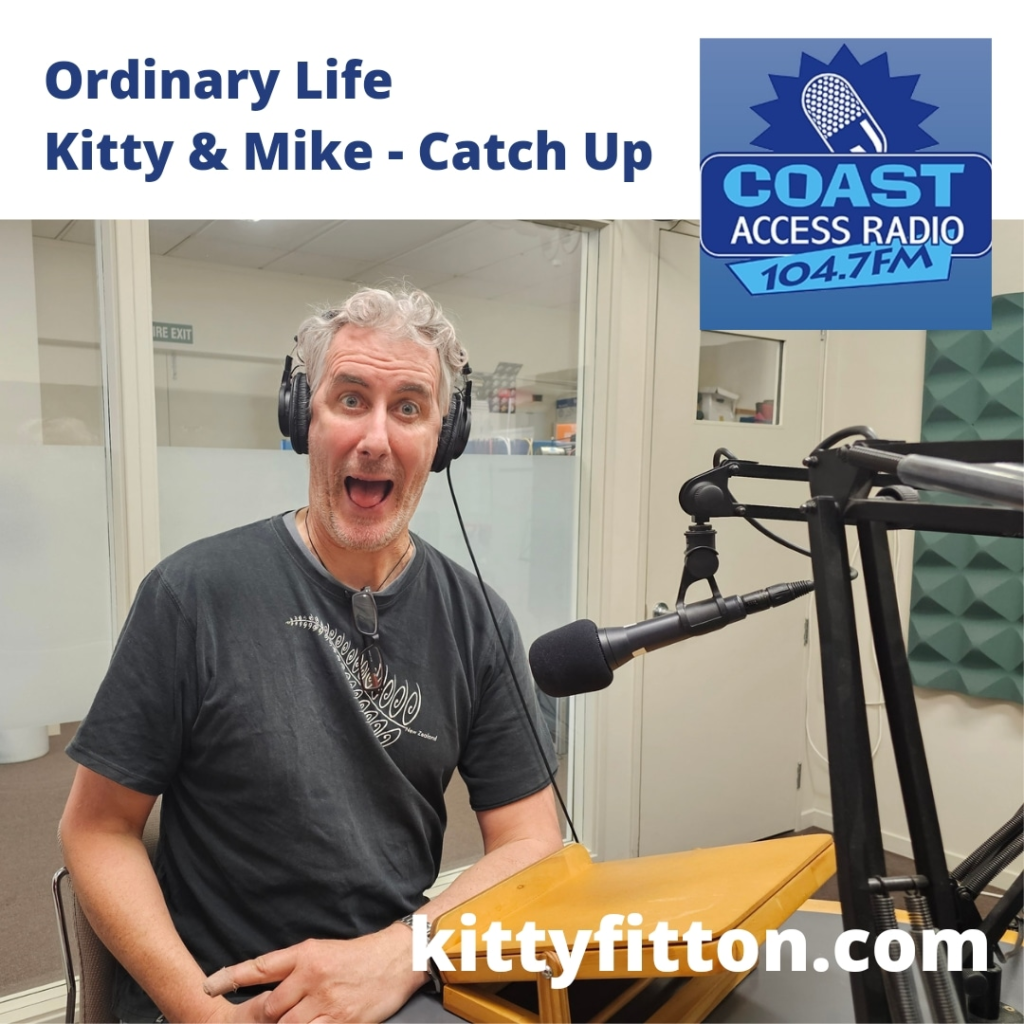 image shows man in mid 50s with grey hair wearing grey tshirt grinning crazily at the camera facing a microphone.